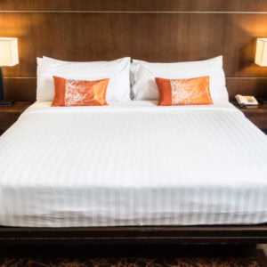 Cama con ropa de cama blanca y cojines naranjas en habitación moderna.